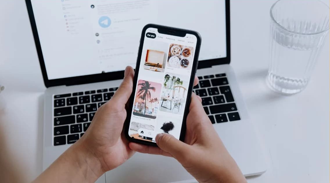 Χέρια κρατούν smartphone μπροστά από ανοιχτό φορητό υπολογιστή σε γραφείο